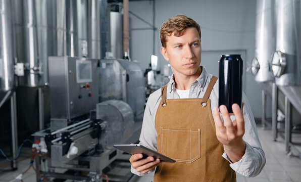 Male brewer inspecting beer can in brewery facility with tablet computer. Concept marking code, labeling and certification of alcoholic beverages - Powered by Adobe