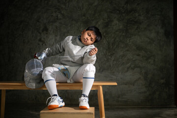A boy in fencing gear sitting on a bench, ready for the épée competition