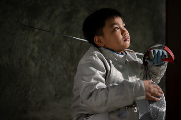 A boy in fencing gear sitting on a bench, ready for the épée competition