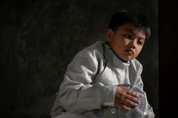 A boy in fencing gear sitting on a bench, ready for the épée competition