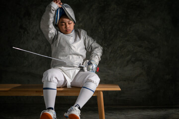 A boy sitting on a bench, taking off his fencing helmet after the épée competition ended