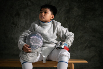 A boy in fencing gear sitting on a bench, ready for the épée competition