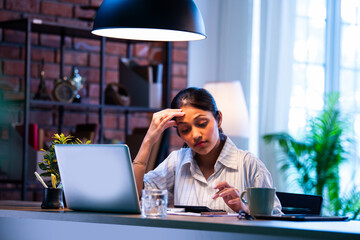 Indian female accountant checking calculations using calculator at desk in cozy office