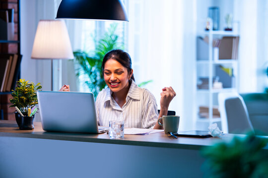 Indian businesswoman shows victory gesture while working on laptop at desk in modern office