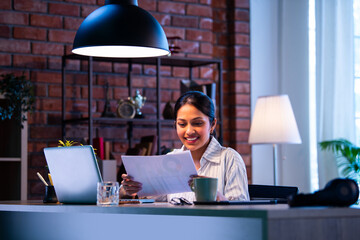 Indian businesswoman looks satisfied after reviewing documents and financial growth at workplace