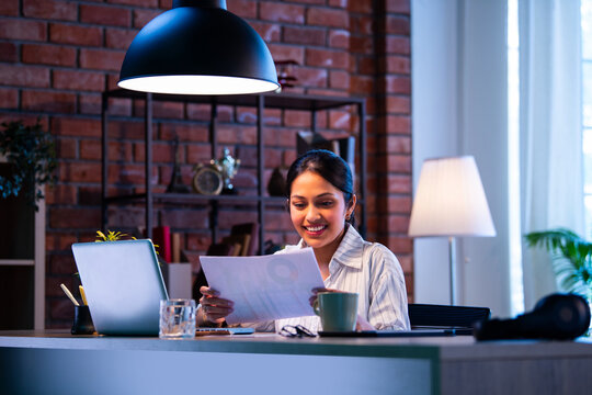 Indian businesswoman looks satisfied after reviewing documents and financial growth at workplace - Powered by Adobe