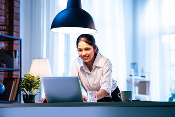Indian businesswoman standing at desk and typing on laptop during work in cozy office