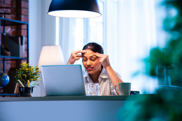 Indian businesswoman feels pressure and headache while working on laptop at modern office desk