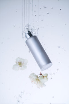 Botella cosm&eacute;tica blanca con flores y agua en fondo minimalista, envase de s&eacute;rum para skincare con dise&ntilde;o limpio y elegante, mockup de frasco cosm&eacute;tico flotando en agua con flores blancas