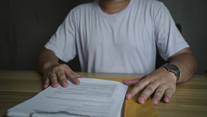 Naklejka premium Man placing hands on a document at a wooden desk. Business, decision-making, or legal review concept. Close-up, focus on hands and paper.