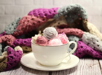 A cup and a saucer with clews balls of yarn wool and crocheted blanket handmade craft bright photo	

