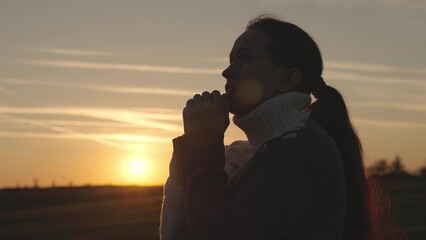 girl praying at sunset in the sky, silhouette of a woman asking for help, reading prayer in sun,...