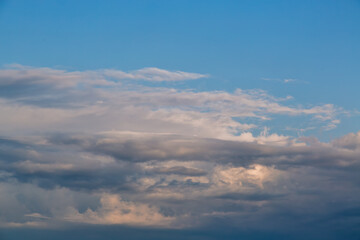 Evening light reflection from the sun on layered clouds in the sky before twilight in pastel tones, a panoramic view of layered clouds in the sky, beautiful clouds in the blue evening sky.