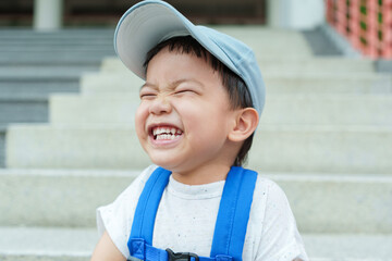 Cheerful Asian Chinese boy sitting on steps smiling big outdoors happy child.
