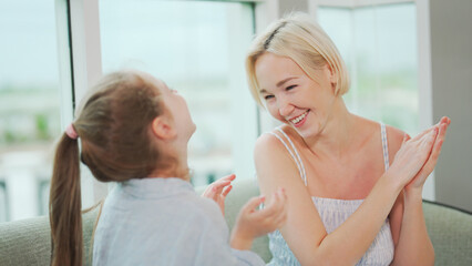 Smiling mother playing clap game with daughter laughing indoors family fun moment.