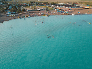 Drone photo, top view of a beach with turquoise sea and many vacationers sunbathing and swimming on a bright summer day.