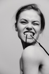 Playful young woman with a cheeky smile biting on her glasses, exuding confidence and joy against a...