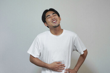 Young Asian man touches his stomach with a relieved expression