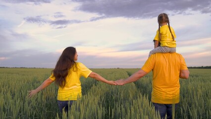 a farmer with his wife and a little kid on his shoulders walks in a green wheat field, a happy...