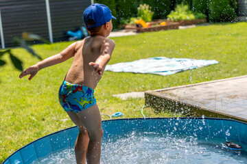 Young boy jumping and splashing water in backyard kiddie pool during sunny day, childhood fun and summer activity