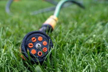 Black and orange garden hose spray nozzle lying on green grass, macro view of irrigation tool for...