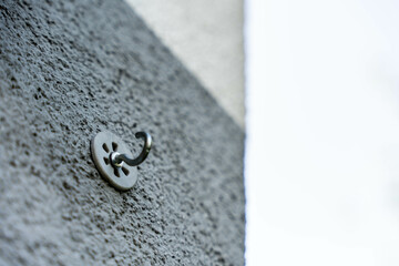 Wall hook screwed into rough exterior plaster, used for supporting outdoor items or structures, close-up composition with bokeh background