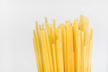 Dry raw spaghetti noodles isolated on white background in close-up view, vertical yellow pasta sticks concept for food theme