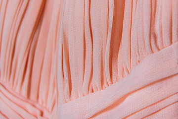 Detailed view of pleated peach fabric texture with soft lighting highlighting garment flow and feminine fashion concept