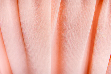 Macro view of peach pleated fabric with soft folds and detailed weave structure representing fashion and textile applications