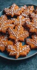 A plate of maple leaf-shaped cookies, decorated with white icing depicting delicate branches, rests on a dark surface