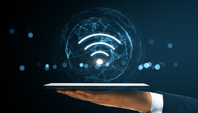Wireless network symbol above digital tablet held by hand with futuristic tech connecting lines on dark background in a business technology concept.
