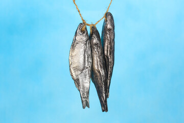Soap shape of dried fish hanging on a rope, blue background.