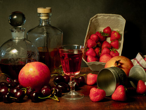 Still life with rose flowers, summer fruits, bottles of wine and a glass of wine. Pomegranate, cherry, sweet cherry, strawberry and watermelon. Alcohol. The still life is stylized as an old painting.