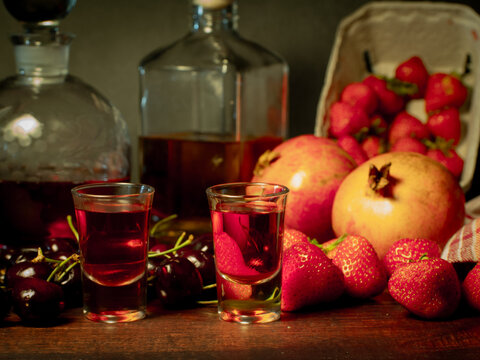 Still life with rose flowers, summer fruits, bottles of wine and a glass of wine. Pomegranate, cherry, sweet cherry, strawberry and watermelon. Alcohol. The still life is stylized as an old painting.