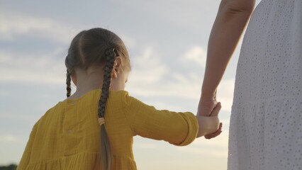 mother holding the hand of a little child against the background of the sky, happy family, daughter...
