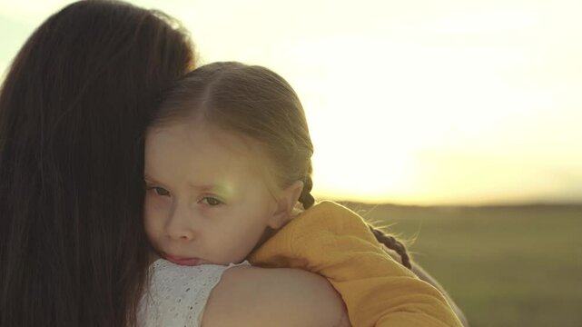 little kid hugs mother in the rays of the sun, happy family at sunset, woman loves child, take motherhood a pleasant feeling, girl daughter with mom on a journey against the sky, custody of baby.