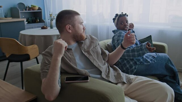 Caucasian man and Black woman annoyed with each other sitting on sofa, squabbling over trivial problem