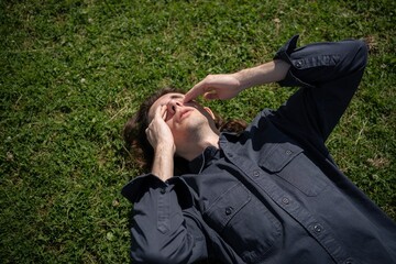 Relaxation under the sun evokes serenity as a young man contemplates life while lying on lush grass...