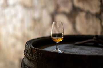 Glass of quality aged wine on a wooden barrel in a stone wine cellar, symbolizing wine tasting and tradition.