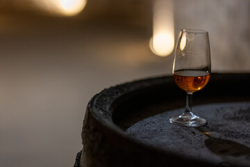 Glass of aged wine on a wooden barrel in a quiet stone wine cellar, capturing the atmosphere of...