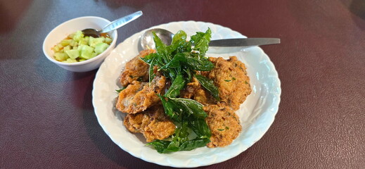 Fried Fish-Paste Balls in a white plate and topped with crispy basil leaves. Thai Fish Cakes placed...