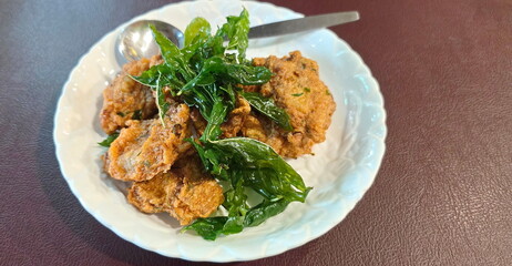 Fried Fried Fish-Paste Balls in a white plate and topped with crispy basil leaves  eat with PLUM Sauce for More Delicious. Thai Fish Cakes placed on a brown table. Groundd Fish with Various Spices,