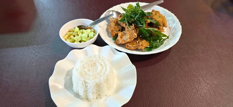 The food set consists of steamed rice on a white dish, fried fish cakes (Clown featherback fish), topped with crispy basil, sweet, spicy, cucumber sauce. Popular menu, eaten with rice or an appetizer.