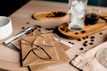 Reading glasses rest on envelopes and notebooks beside a cup of coffee. Cozy workspace setup with...