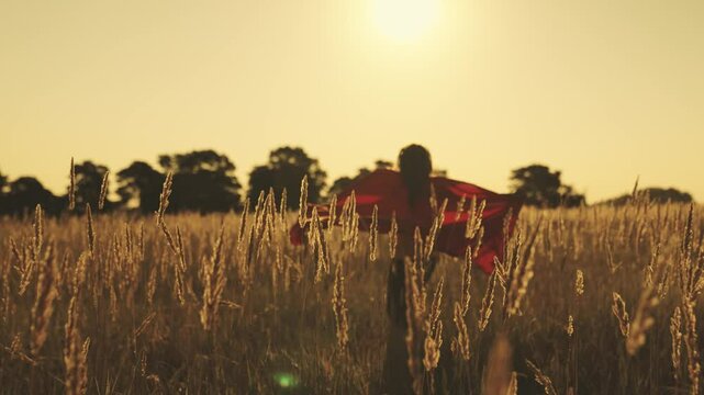happy girl play superheroes they run across green field in red cloak, cloak flutters in wind. children's games and dreams. Slow motion. teenager dreams of becoming superhero. young girls in red cloak.