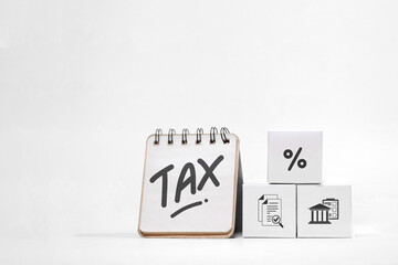 A notepad with TAX written on it sits next to blocks with financial icons, representing tax documentation and calculation.