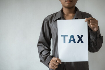 Person in grey shirt holding white paper with the word TAX printed on it