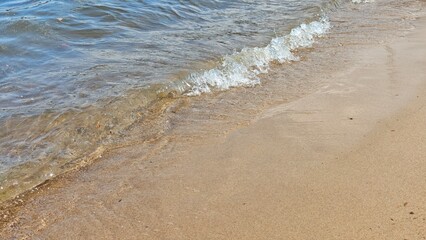 Close-up of gentle sea waves washing onto sandy beach under sunlight on a calm day. Represents relaxation, summer vacation, and peaceful nature concept