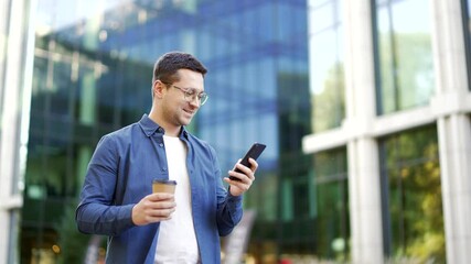 Happy handsome businessman walking on street looking at phone outside modern office building with cup of coffee in hand. Smiling confident man in blue shirt enjoys a walk in an urban city setting - Powered by Adobe