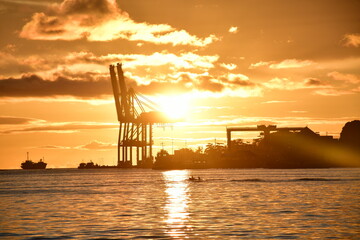 Obraz premium Golden sunset over the sea with a crane silhouette, a boat, and reflections on the water.
